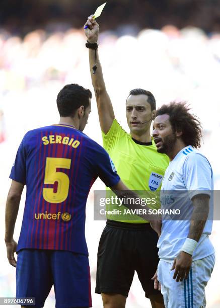 Referee Jose Maria Sanchez Martinez shows a yellow card to Real Madrid's Brazilian defender Marcelo next to Barcelona's Spanish midfielder Sergio...