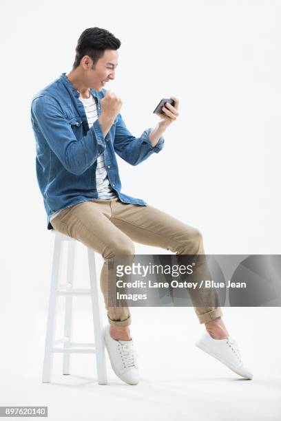 cheerful young man holding a smart phone - asian man sitting at desk stock pictures, royalty-free photos & images