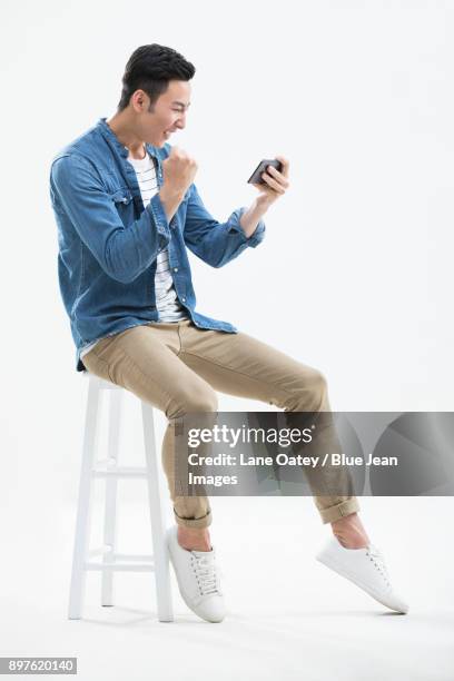 cheerful young man holding a smart phone - asian man sitting casual imagens e fotografias de stock