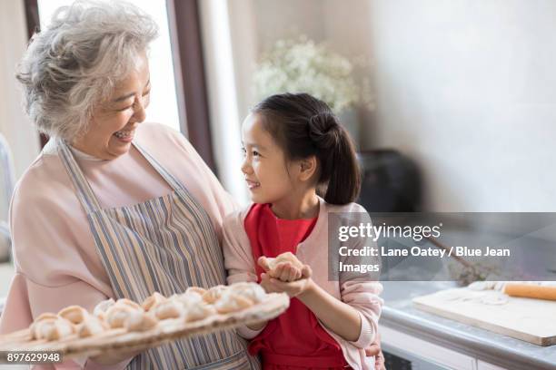 cheerful granddaughter and grandmother making dumplings in kitchen - asian cooking stock-fotos und bilder