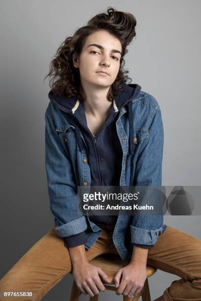 girl in her late teens sitting on a stool wearing a jeans jacket in front of a gray background, portrait.