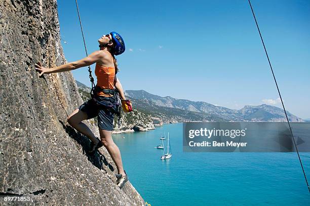 woman rock climbing, bay in background - sardinien stock-fotos und bilder