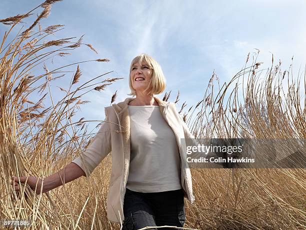 mature woman walking in reeds - une seule femme d'âge mûr photos et images de collection