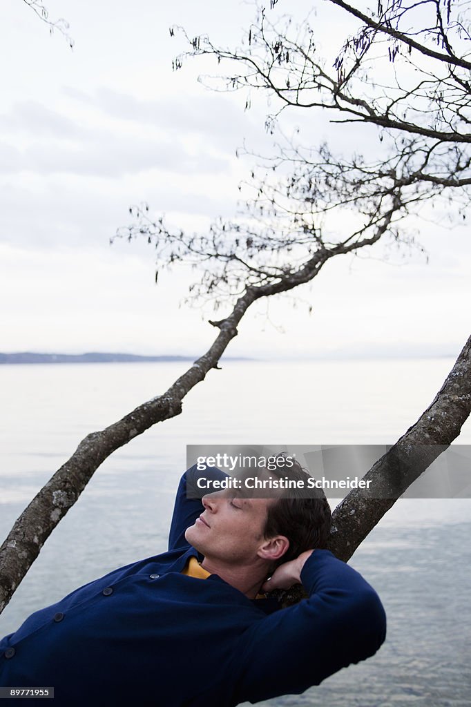 Man resting on tree branch at lake