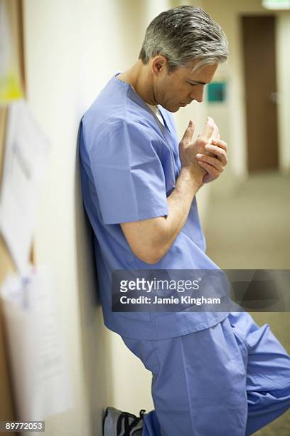 tired male surgeon leaning on wall - overdoing stock pictures, royalty-free photos & images
