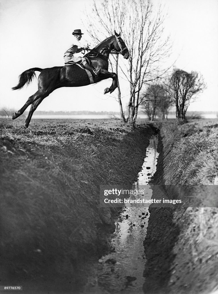 The german show jumper Axel Holst during a jump over a moat at a morning ride across the fields. Photograph. Around 1930.