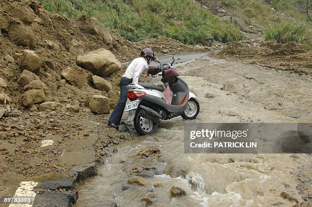 Man pushes his motorcycle on a damaged and flooded road in the village of Meishan in Chiayi county, southern Taiwan, on August 14, 2009. Rescuers in...