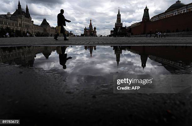 Man is refelcted in a puddle while walking across Red Square in central Moscow on August 14, 2009. Muscovites are encountering intermittent sun and...