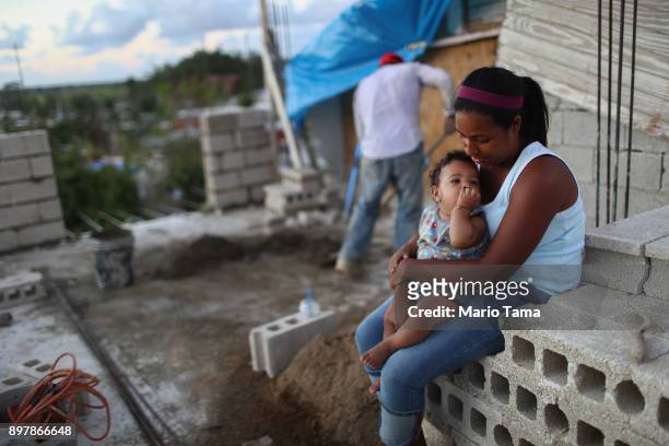 Mother Isamar holds her baby Saniel, 9 months, as husband Samuel mixes cement at their makeshift home, under reconstruction, after being mostly...