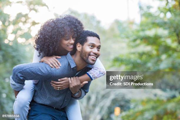 playful young woman rides piggyback on her boyfriend's back - park couple piggyback stock pictures, royalty-free photos & images