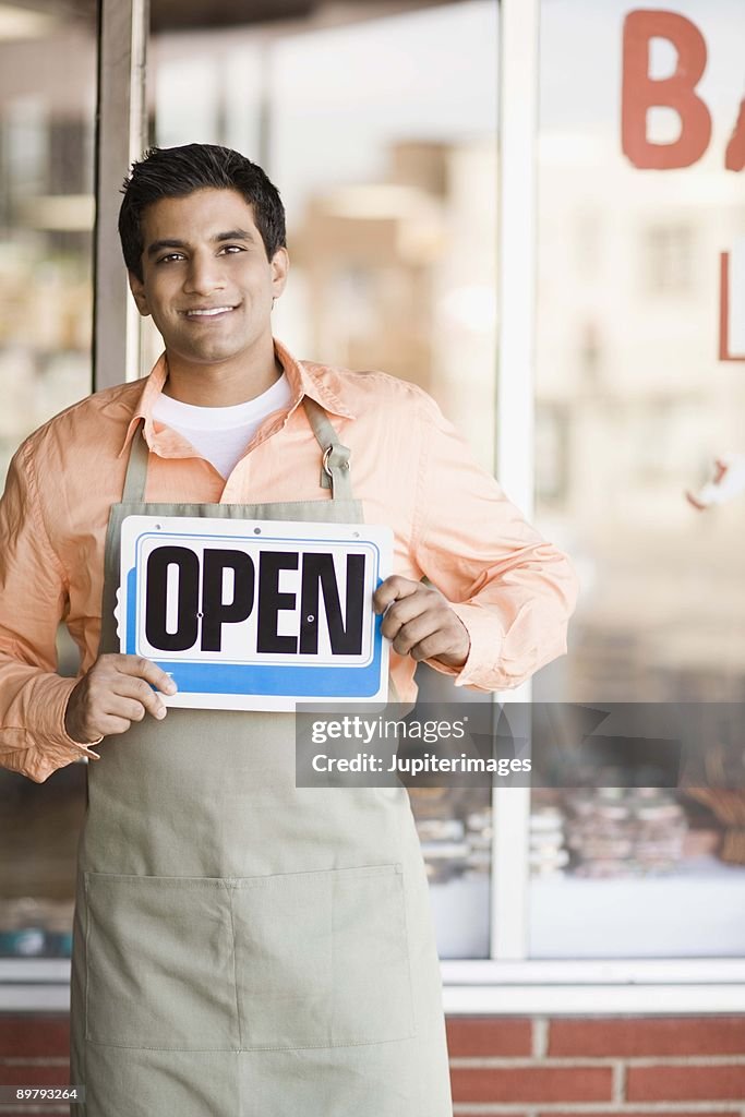 Shopkeeper smiling by storefront with open sign