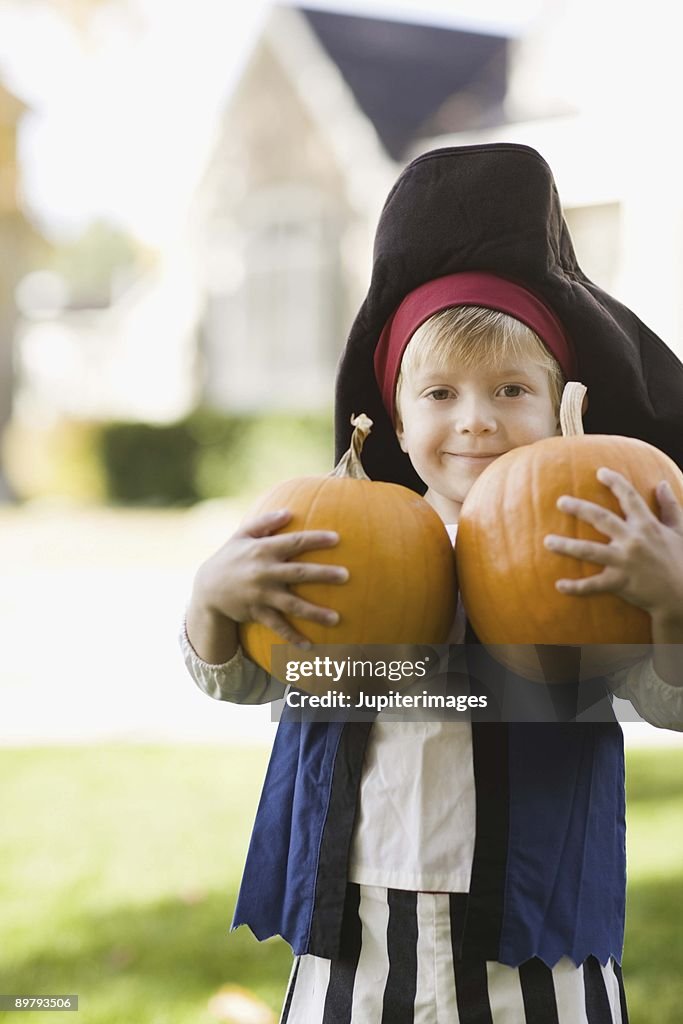 Boy in Halloween costume holding pumpkins