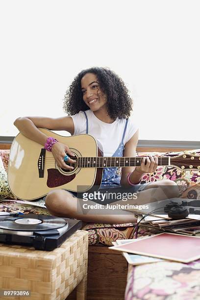 teenage girl playing acoustic guitar indoors - a woman modelling a trouser suit blends in with a matching background of floral print cushions stockfoto's en -beelden