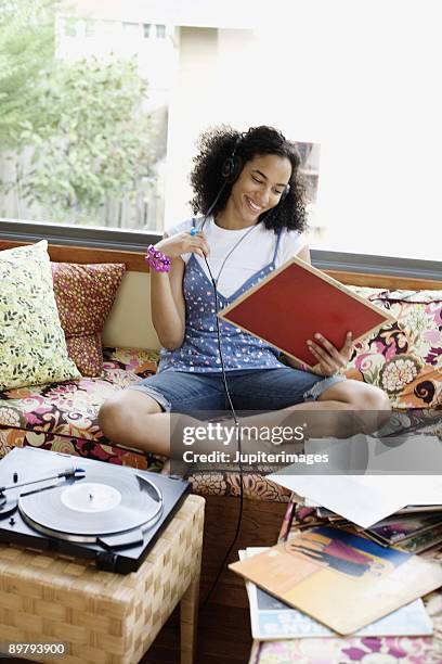 teenage girl listening to headphones and looking at records indoors - a woman modelling a trouser suit blends in with a matching background of floral print cushions stockfoto's en -beelden