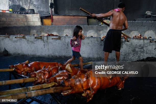 Child skips over bamboo skewered roasted pigs at a 'lechon' grill on Christmas Eve in Manila on December 24, 2017. Locally known as 'lechon' or...