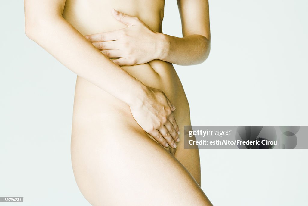 Nude woman covering body with hands, mid section