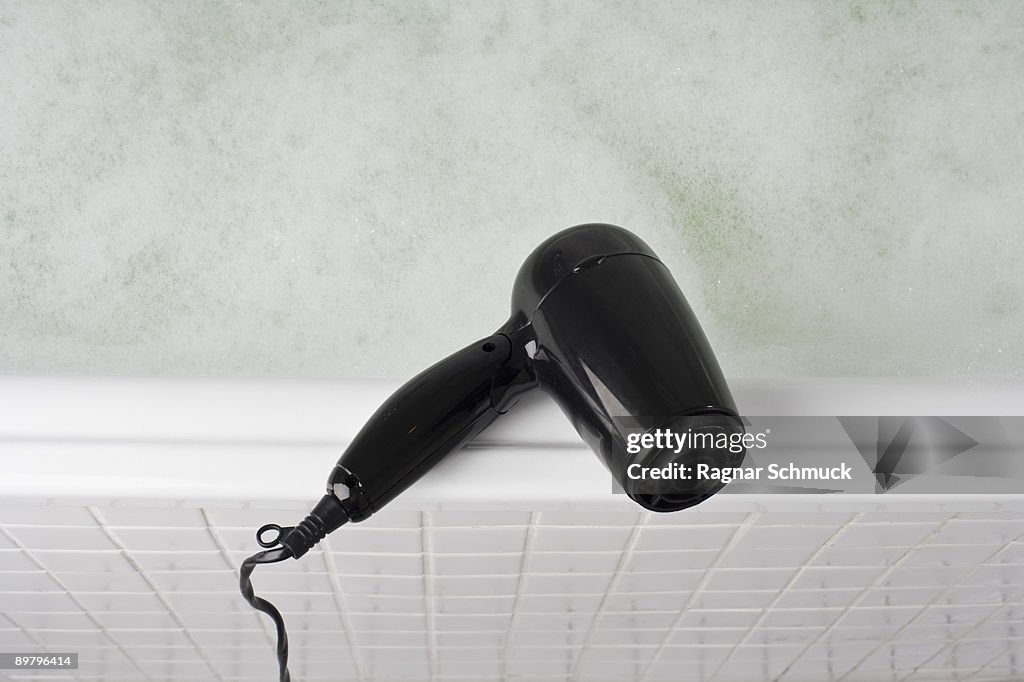 A hair dryer balancing on the edge of a full bathtub