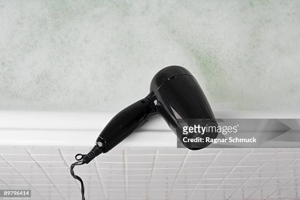a hair dryer balancing on the edge of a full bathtub - hair dryer foto e immagini stock