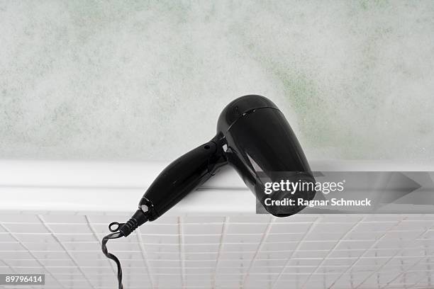 a hair dryer balancing on the edge of a full bathtub - haardroger stockfoto's en -beelden