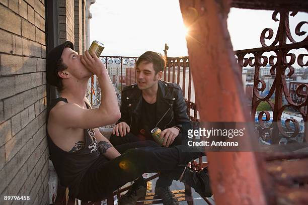 two young men sitting on a fire escape drinking beer - punk person stock-fotos und bilder