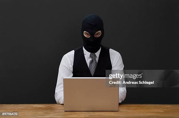 a man wearing a  balaclava and using a laptop - bivakmuts stockfoto's en -beelden