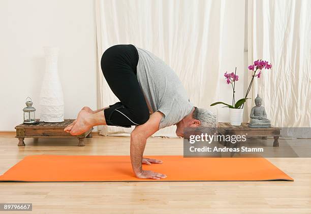 a senior man doing yoga, crow pose - senior yoga stock-fotos und bilder