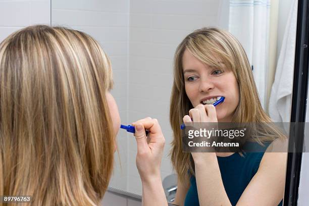 a young woman brushing her teeth in front of a bathroom mirror - bad bangs stock-fotos und bilder