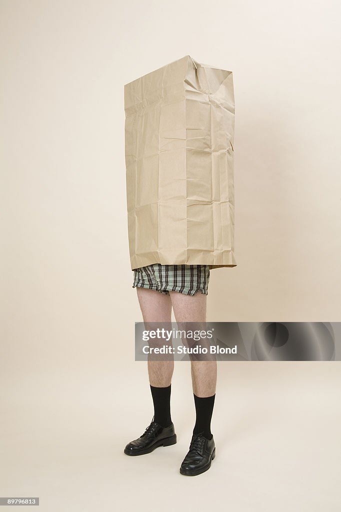 A semi-dressed man wearing a large paper bag