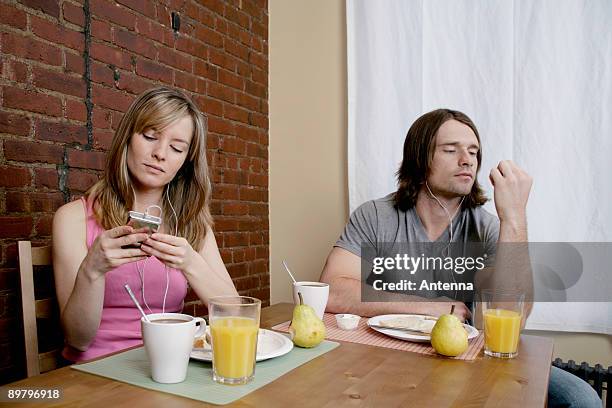 a young couple sitting at breakfast listening to mp3 players - mp3 juices 個照片及圖片檔