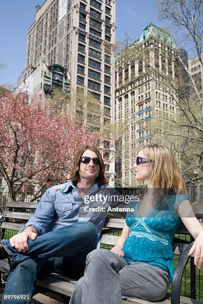 a young couple wearing sunglasses and sitting on a park bench together, central park, new york city - couple central park stockfoto's en -beelden