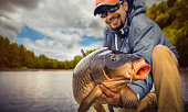 Fishing backgrounds. Young man hold big carp in his hands.