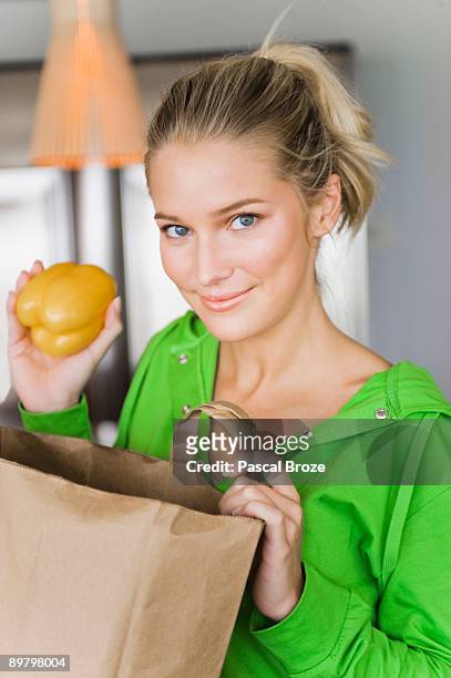 portrait of a woman taking out yellow pepper from a paper bag - gele paprika stockfoto's en -beelden