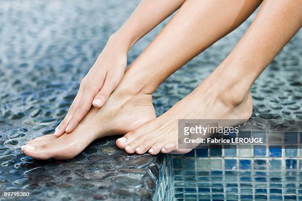 woman rubbing her foot at the poolside - beautiful people stock-fotos und bilder