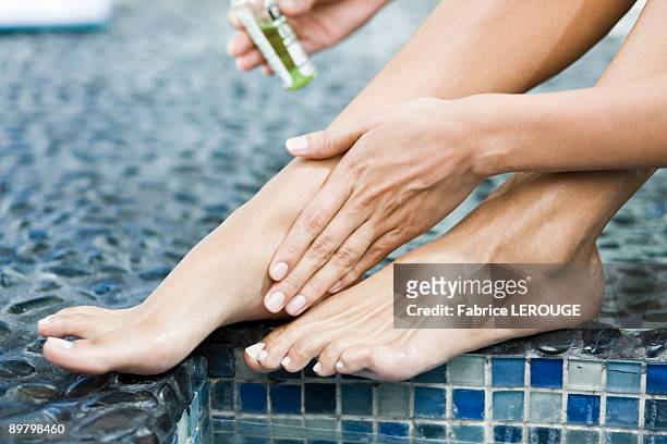 woman applying oil on her legs at the poolside - spa treatment photos et images de collection