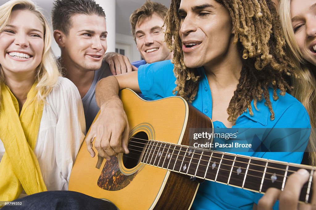 Man sitting with his friends and playing a guitar