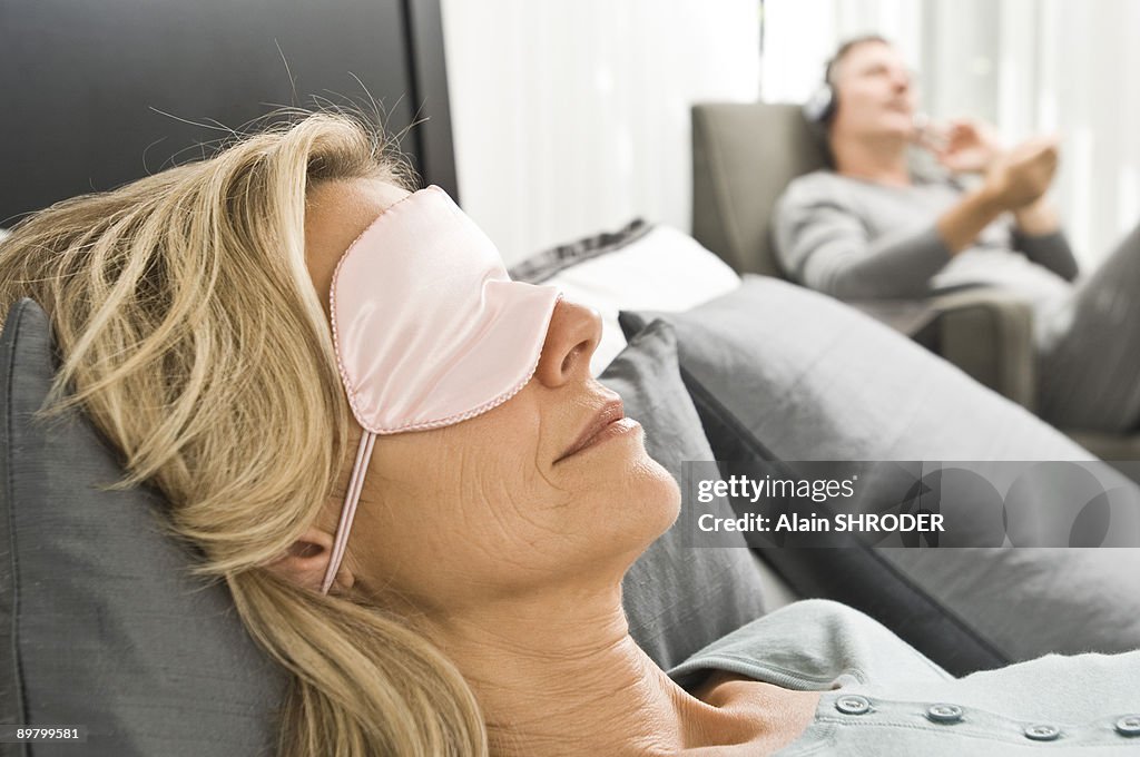 Woman wearing an eye mask and her husband listening to music in the background