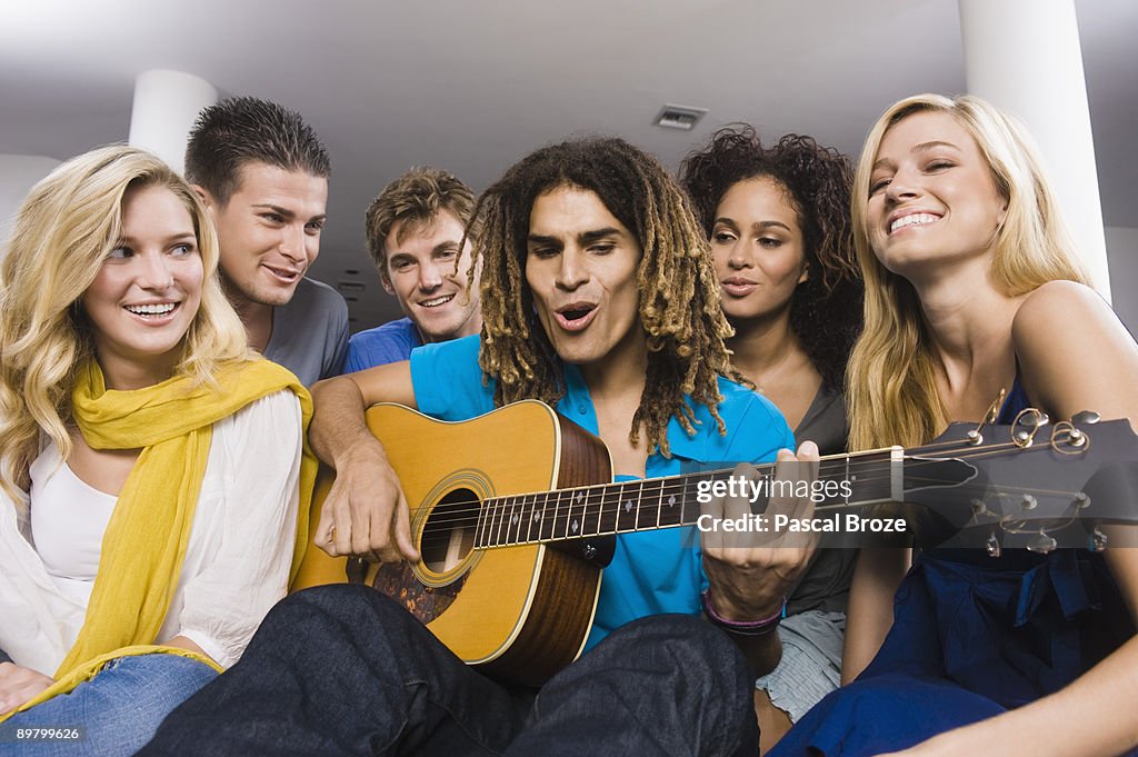 Man sitting with his friends and playing a guitar