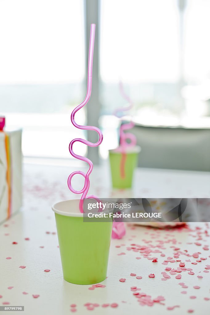 Disposable glasses with drinking straws and a birthday present on a table