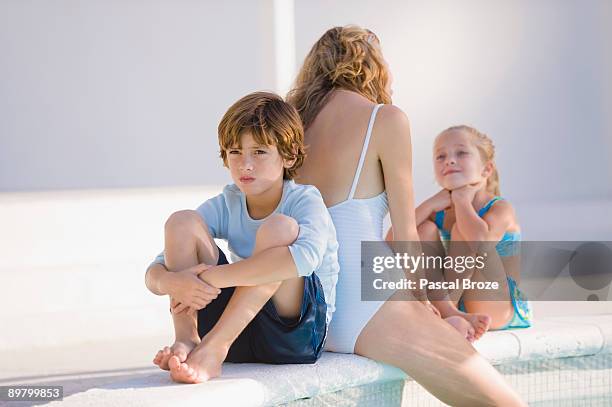 woman with her two children sitting at the poolside - ignorieren stock-fotos und bilder