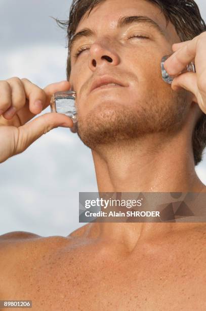 man rubbing ice cubes on his cheeks - frotar fotografías e imágenes de stock