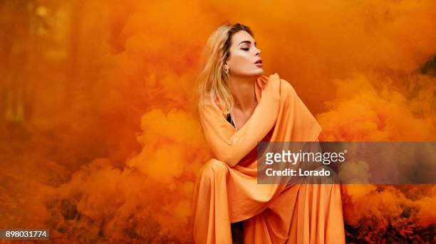 beautiful young blond female woman dancing and posing in orange smoke in outdoor countryside setting - fashion orange colour stock pictures, royalty-free photos & images