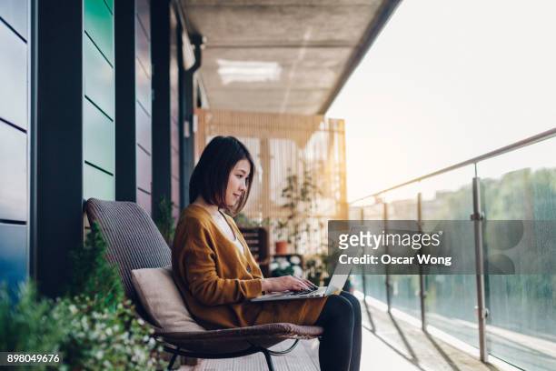 young woman working on laptop in balcony - werk laptop buiten stockfoto's en -beelden