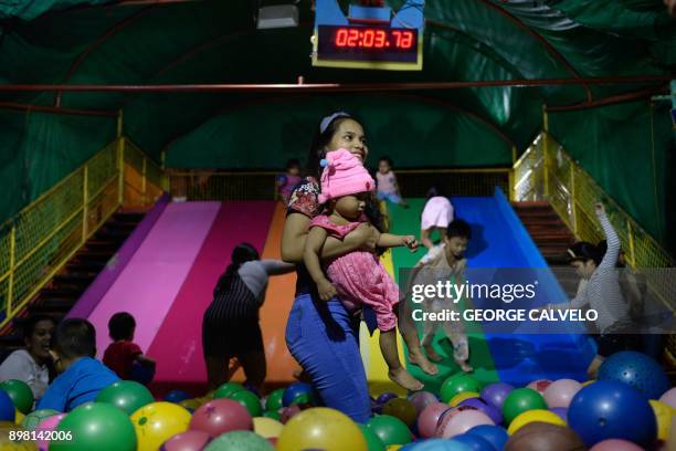 This picture taken on December 24, 2017 shows a woman carrying a child inside a ball pit on Christmas Eve at an amusement park in Antipolo, east of...