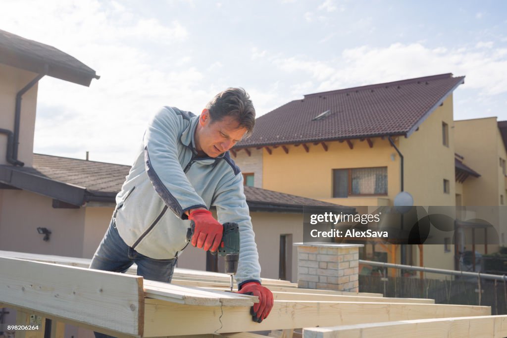 Male constructor drilling wooden chalet roof