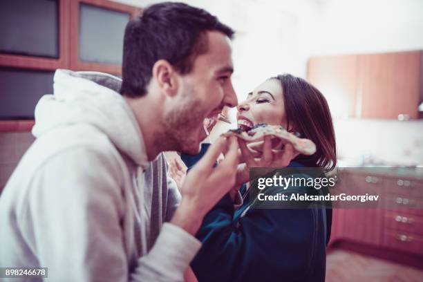 young smiling couple eat pizza in the kitchen at home - sharing pizza stock pictures, royalty-free photos & images