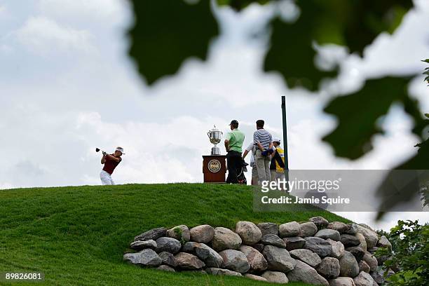 Soren Kjeldsen of Denmark hits his tee shot as Lucas Glover looks on alongside the Wanamaker Trophy on the first hole during the final round of the...
