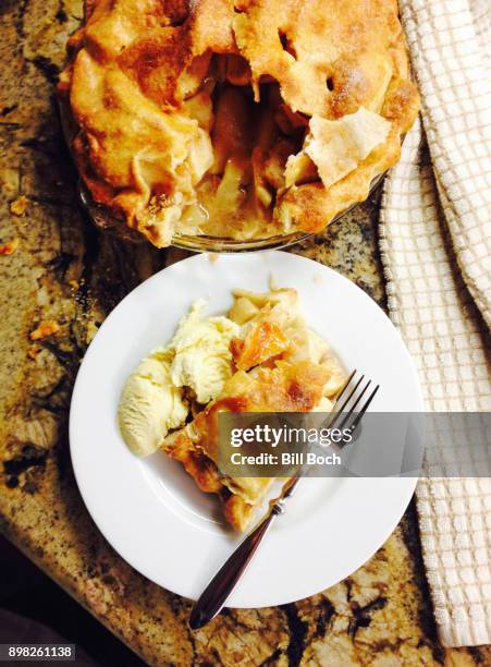 slice of apple pie with vanilla ice cream on a plate with a fork, on a kitchen counter, with the whole pie in the background - apple pie a la mode stock pictures, royalty-free photos & images