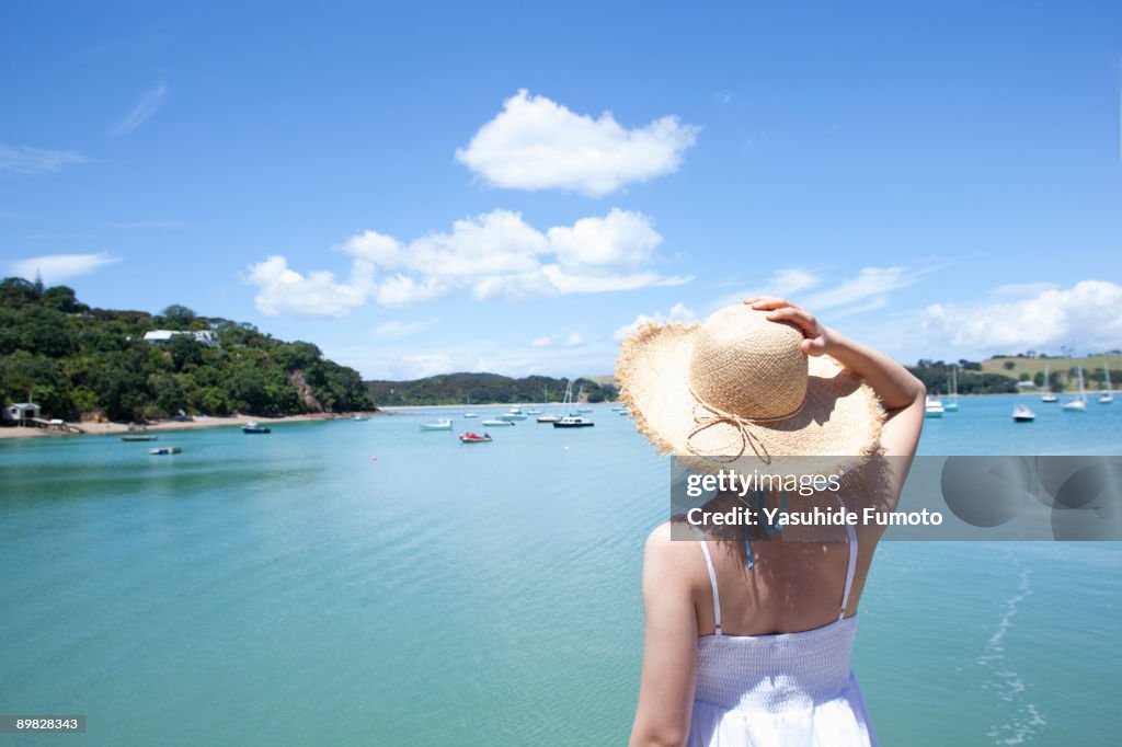 A woman with a straw hat looking at the sea.