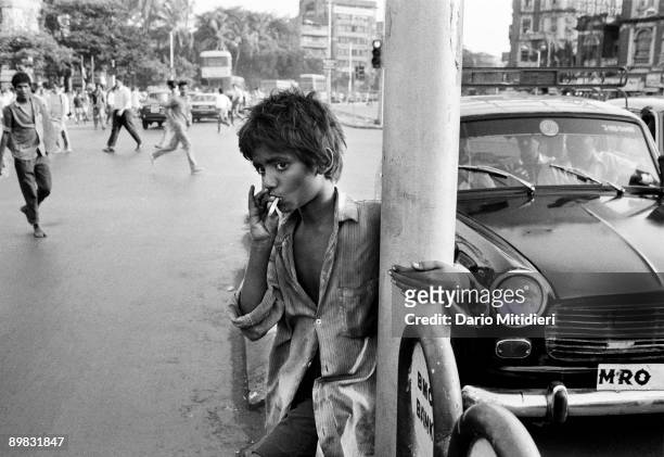 Sangay, a street child from Delhi, smoking the remainder of a cigarette which he found in the street outside Victoria Terminus station in Bombay,...