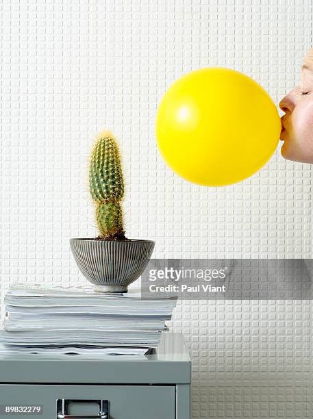lady blowing up balloon next to cactus - inflate stock-fotos und bilder